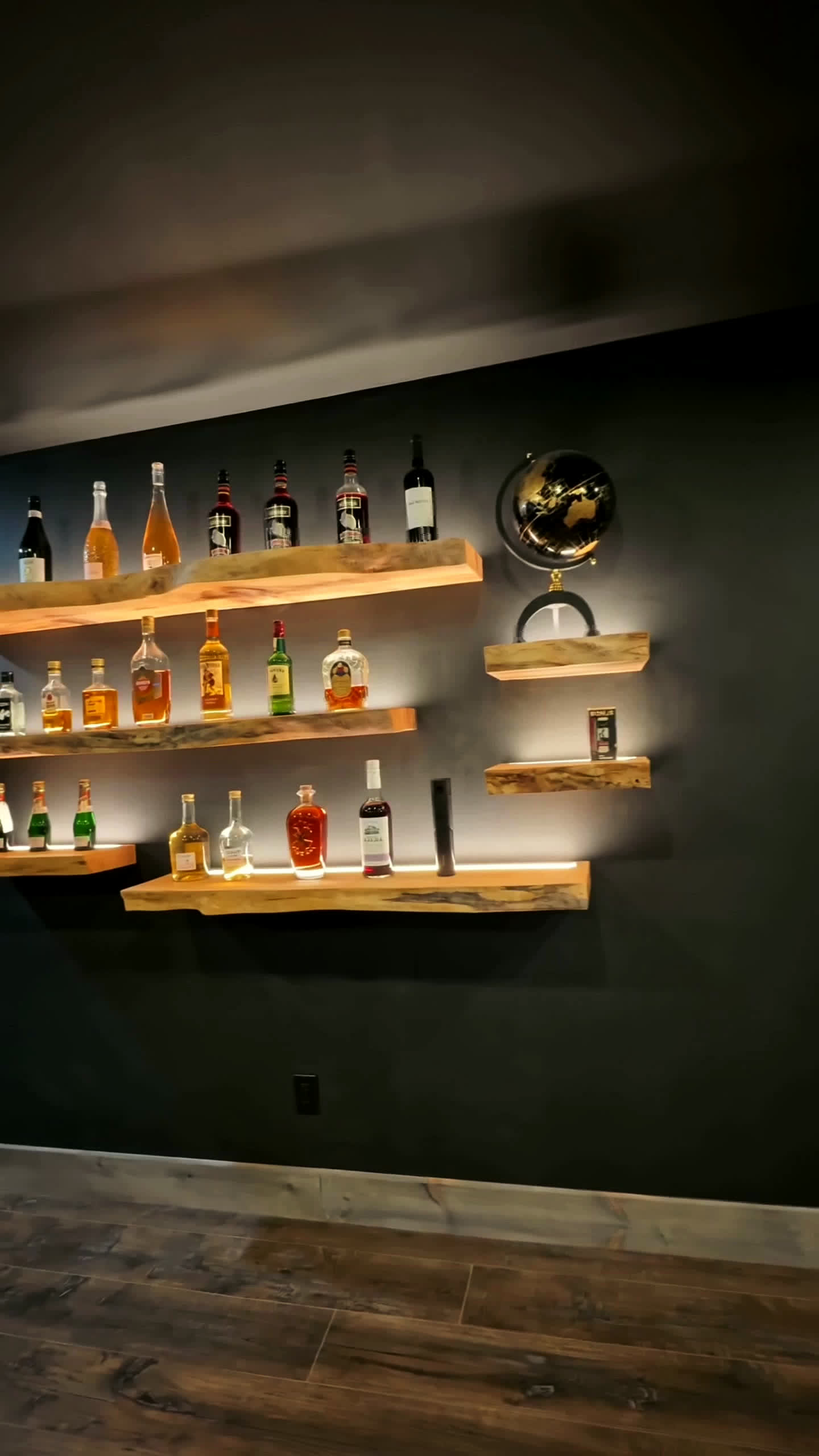 Backlit live-edge whisky shelves in a finished basement lounge
